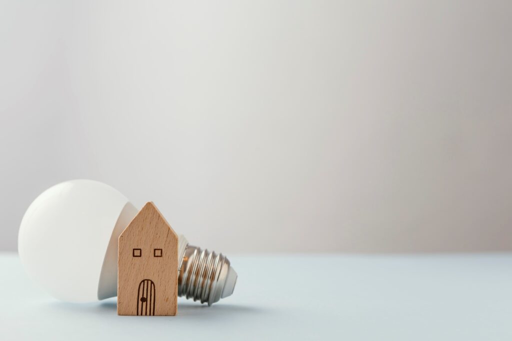 A wooden house figurine and a light bulb on the table in the concept of 'Changing Address and Updating Utilities After Moving to Richmond'.